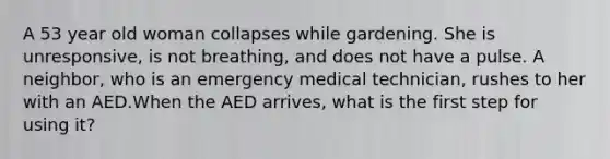 A 53 year old woman collapses while gardening. She is unresponsive, is not breathing, and does not have a pulse. A neighbor, who is an emergency medical technician, rushes to her with an AED.When the AED arrives, what is the first step for using it?