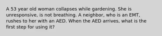 A 53 year old woman collapses while gardening. She is unresponsive, is not breathing. A neighbor, who is an EMT, rushes to her with an AED. When the AED arrives, what is the first step for using it?