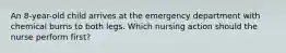 An 8-year-old child arrives at the emergency department with chemical burns to both legs. Which nursing action should the nurse perform first?