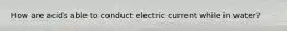 How are acids able to conduct electric current while in water?