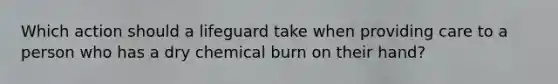 Which action should a lifeguard take when providing care to a person who has a dry chemical burn on their hand?