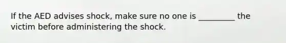 If the AED advises shock, make sure no one is _________ the victim before administering the shock.