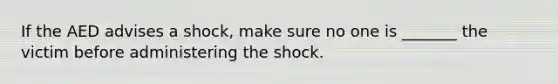 If the AED advises a shock, make sure no one is _______ the victim before administering the shock.