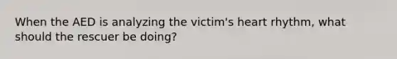 When the AED is analyzing the victim's heart rhythm, what should the rescuer be doing?