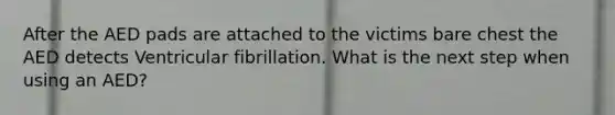 After the AED pads are attached to the victims bare chest the AED detects Ventricular fibrillation. What is the next step when using an AED?