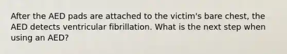 After the AED pads are attached to the victim's bare chest, the AED detects ventricular fibrillation. What is the next step when using an AED?