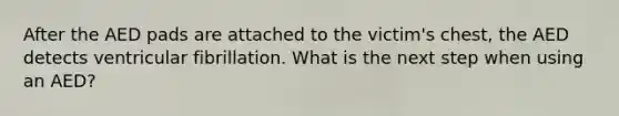 After the AED pads are attached to the victim's chest, the AED detects ventricular fibrillation. What is the next step when using an AED?