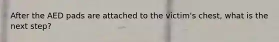 After the AED pads are attached to the victim's chest, what is the next step?