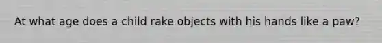 At what age does a child rake objects with his hands like a paw?