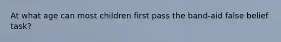 At what age can most children first pass the band-aid false belief task?