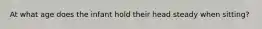 At what age does the infant hold their head steady when sitting?
