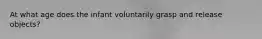 At what age does the infant voluntarily grasp and release objects?