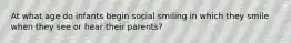 At what age do infants begin social smiling in which they smile when they see or hear their parents?