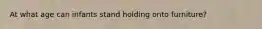 At what age can infants stand holding onto furniture?