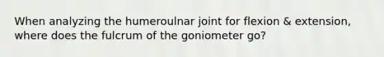 When analyzing the humeroulnar joint for flexion & extension, where does the fulcrum of the goniometer go?