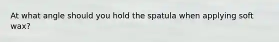 At what angle should you hold the spatula when applying soft wax?