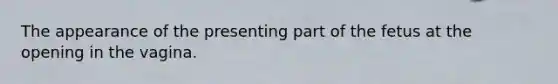 The appearance of the presenting part of the fetus at the opening in the vagina.
