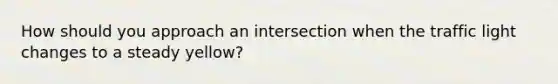 How should you approach an intersection when the traffic light changes to a steady yellow?