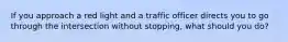 If you approach a red light and a traffic officer directs you to go through the intersection without stopping, what should you do?