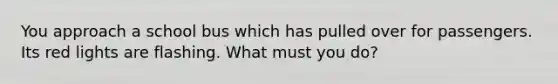 You approach a school bus which has pulled over for passengers. Its red lights are flashing. What must you do?