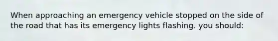 When approaching an emergency vehicle stopped on the side of the road that has its emergency lights flashing. you should: