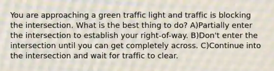 You are approaching a green traffic light and traffic is blocking the intersection. What is the best thing to do? A)Partially enter the intersection to establish your right-of-way. B)Don't enter the intersection until you can get completely across. C)Continue into the intersection and wait for traffic to clear.