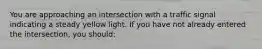 You are approaching an intersection with a traffic signal indicating a steady yellow light. If you have not already entered the intersection, you should: