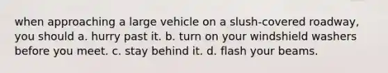 when approaching a large vehicle on a slush-covered roadway, you should a. hurry past it. b. turn on your windshield washers before you meet. c. stay behind it. d. flash your beams.