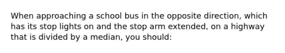 When approaching a school bus in the opposite direction, which has its stop lights on and the stop arm extended, on a highway that is divided by a median, you should: