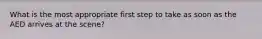 What is the most appropriate first step to take as soon as the AED arrives at the scene?
