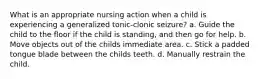 What is an appropriate nursing action when a child is experiencing a generalized tonic-clonic seizure? a. Guide the child to the floor if the child is standing, and then go for help. b. Move objects out of the childs immediate area. c. Stick a padded tongue blade between the childs teeth. d. Manually restrain the child.