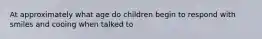 At approximately what age do children begin to respond with smiles and cooing when talked to