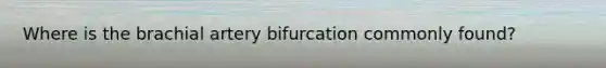 Where is the brachial artery bifurcation commonly found?