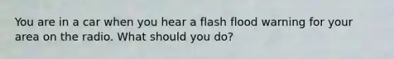 You are in a car when you hear a flash flood warning for your area on the radio. What should you do?