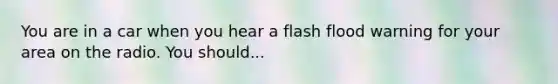 You are in a car when you hear a flash flood warning for your area on the radio. You should...