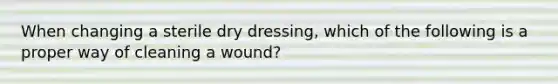 When changing a sterile dry dressing, which of the following is a proper way of cleaning a wound?