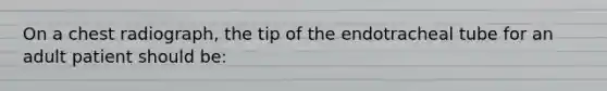 On a chest radiograph, the tip of the endotracheal tube for an adult patient should be: