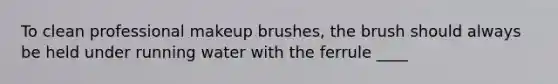 To clean professional makeup brushes, the brush should always be held under running water with the ferrule ____