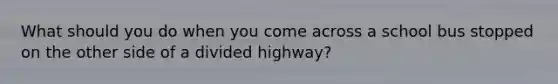 What should you do when you come across a school bus stopped on the other side of a divided highway?