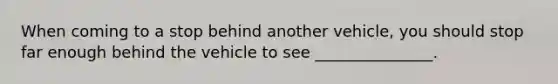 When coming to a stop behind another vehicle, you should stop far enough behind the vehicle to see _______________.