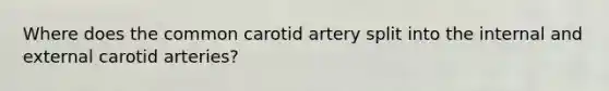 Where does the common carotid artery split into the internal and external carotid arteries?