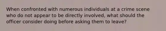 When confronted with numerous individuals at a crime scene who do not appear to be directly involved, what should the officer consider doing before asking them to leave?