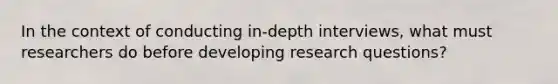 In the context of conducting in-depth interviews, what must researchers do before developing research questions?