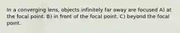 In a converging lens, objects infinitely far away are focused A) at the focal point. B) in front of the focal point. C) beyond the focal point.