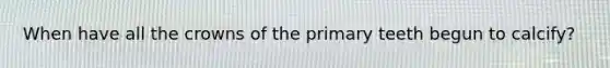 When have all the crowns of the primary teeth begun to calcify?