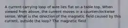 A current carrying loop of wire lies flat on a table top. When viewed from above, the current moves in a counterclockwise sense. What is the direction of the magnetic field caused by this current, outside the loop? The magnetic field