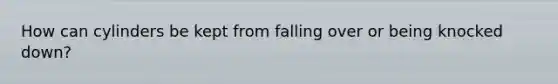 How can cylinders be kept from falling over or being knocked down?