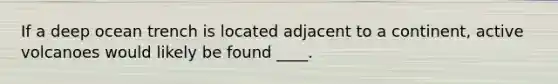 If a deep ocean trench is located adjacent to a continent, active volcanoes would likely be found ____.