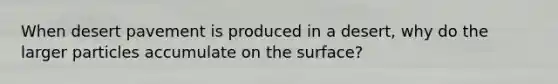 When desert pavement is produced in a desert, why do the larger particles accumulate on the surface?