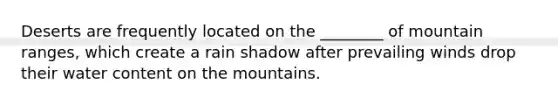 Deserts are frequently located on the ________ of mountain ranges, which create a rain shadow after prevailing winds drop their water content on the mountains.